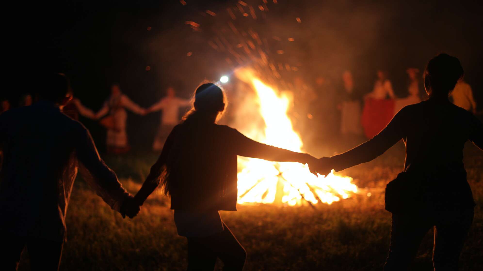 Eine Gruppe Menschen tanzt am 30.04. nachts um ein riesiges Lagerfeuer.