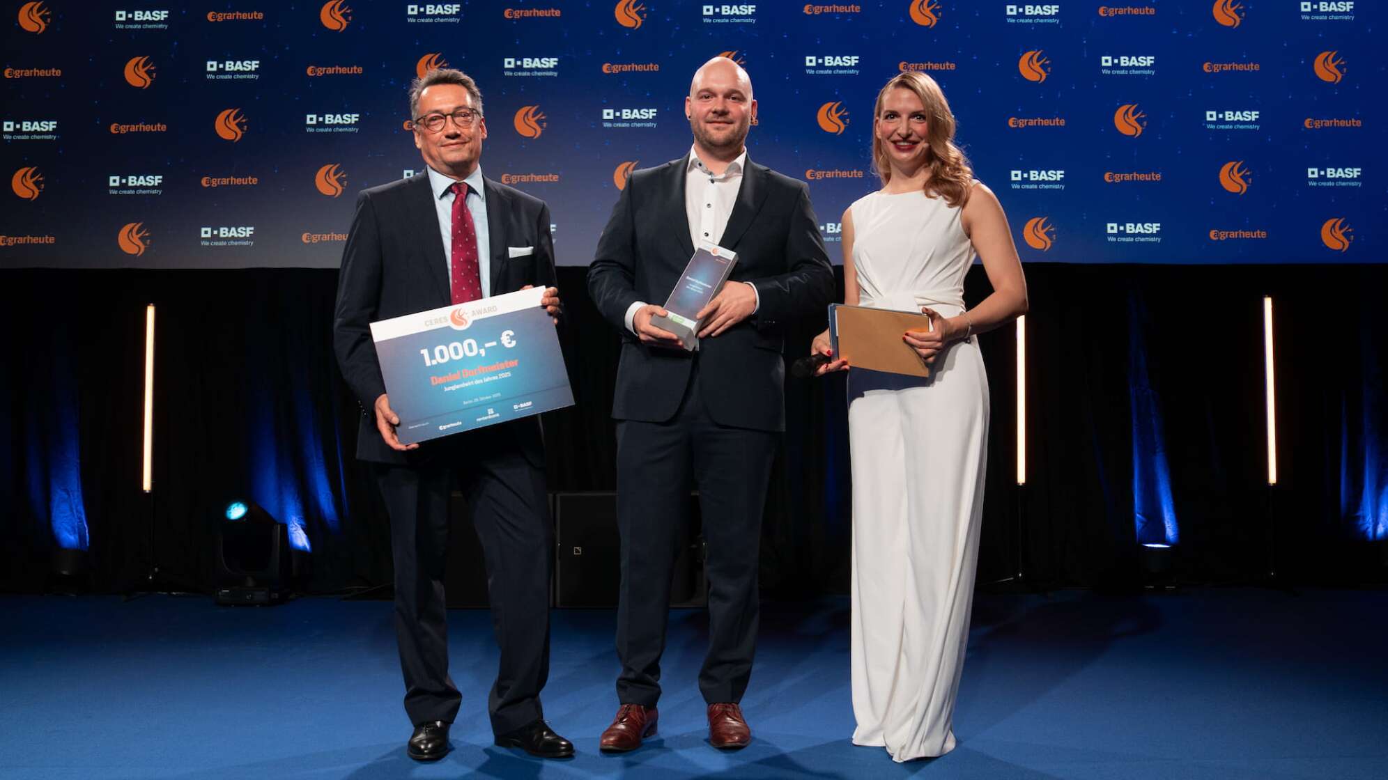 Der Junglandwirt des Jahres 2025 Daniel Dorfmeister (Mitte) mit Markus Röser (Kategoriepartner BASF) und Moderatorin Janine Mehner. Foto: Charlotte Schmitz