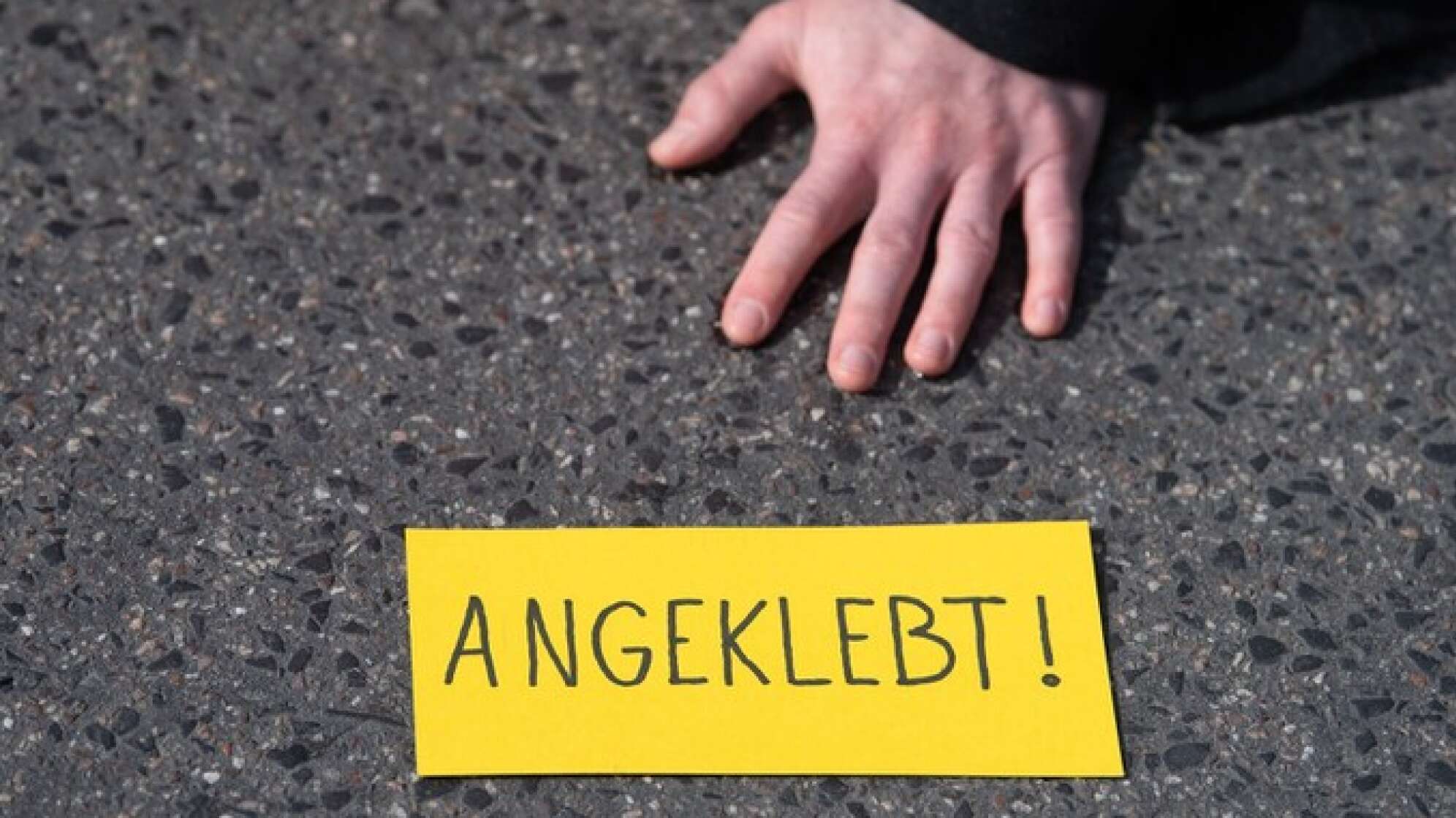Hand am Asphalt festgeklebt