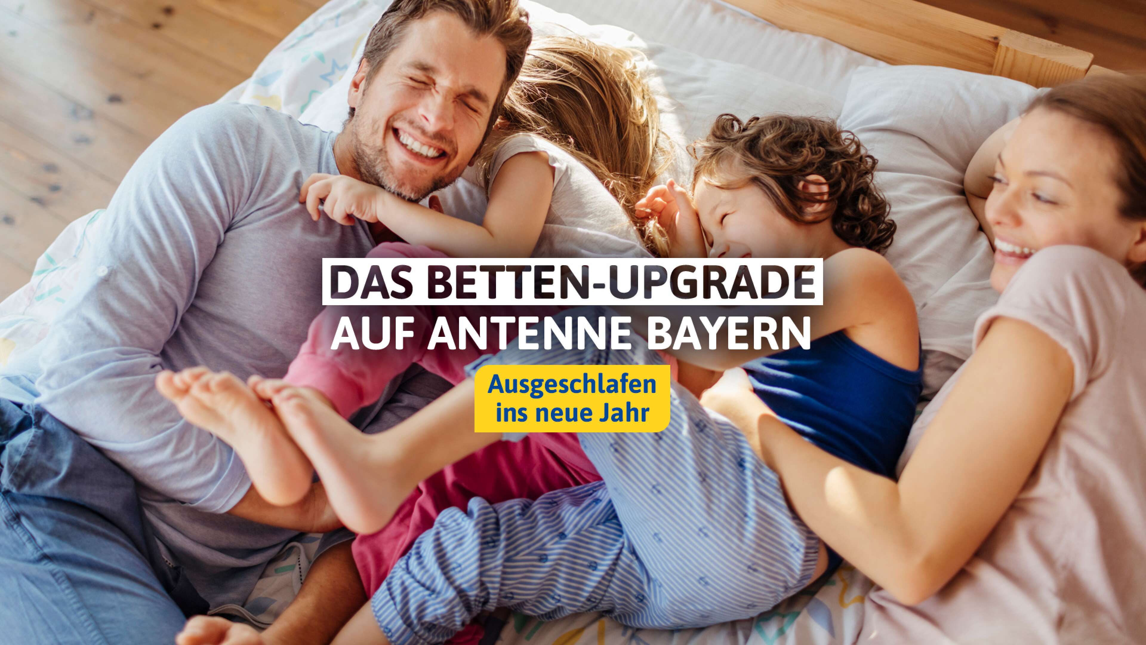 eine glücklich lachende Familie liegt auf einem Bett, dazu der Text