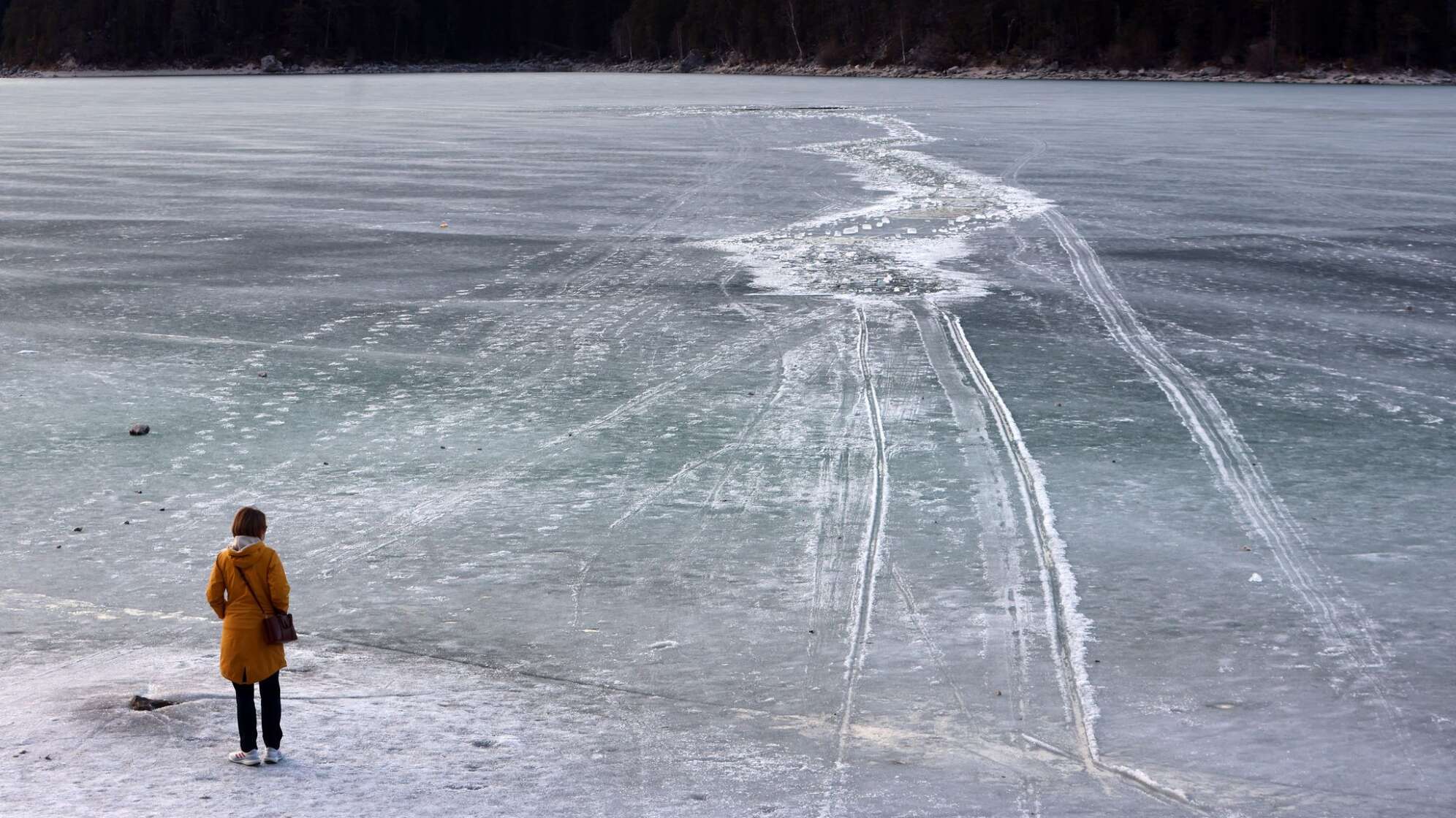 Eine Frau steht am zugefrorenem See nahe einer Einbruchstelle