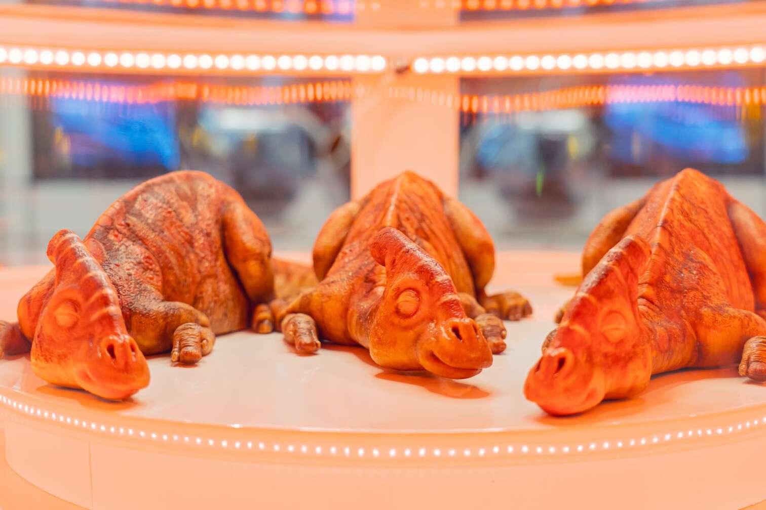 Detailaufnahme von drei Dinosaurierbabys in einem Inkubator der Jurassic World Ausstellung, umgeben von warmem Licht