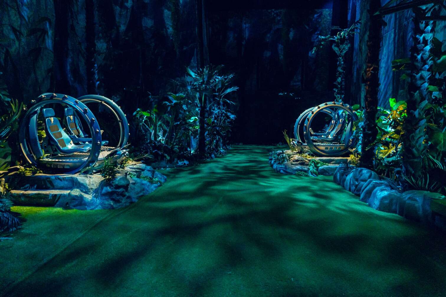 Zwei Jurassic World Gyrosphere-Fahrzeuge in einer detailreichen Dschungelkulisse, umgeben von tropischen Pflanzen und künstlichem Licht