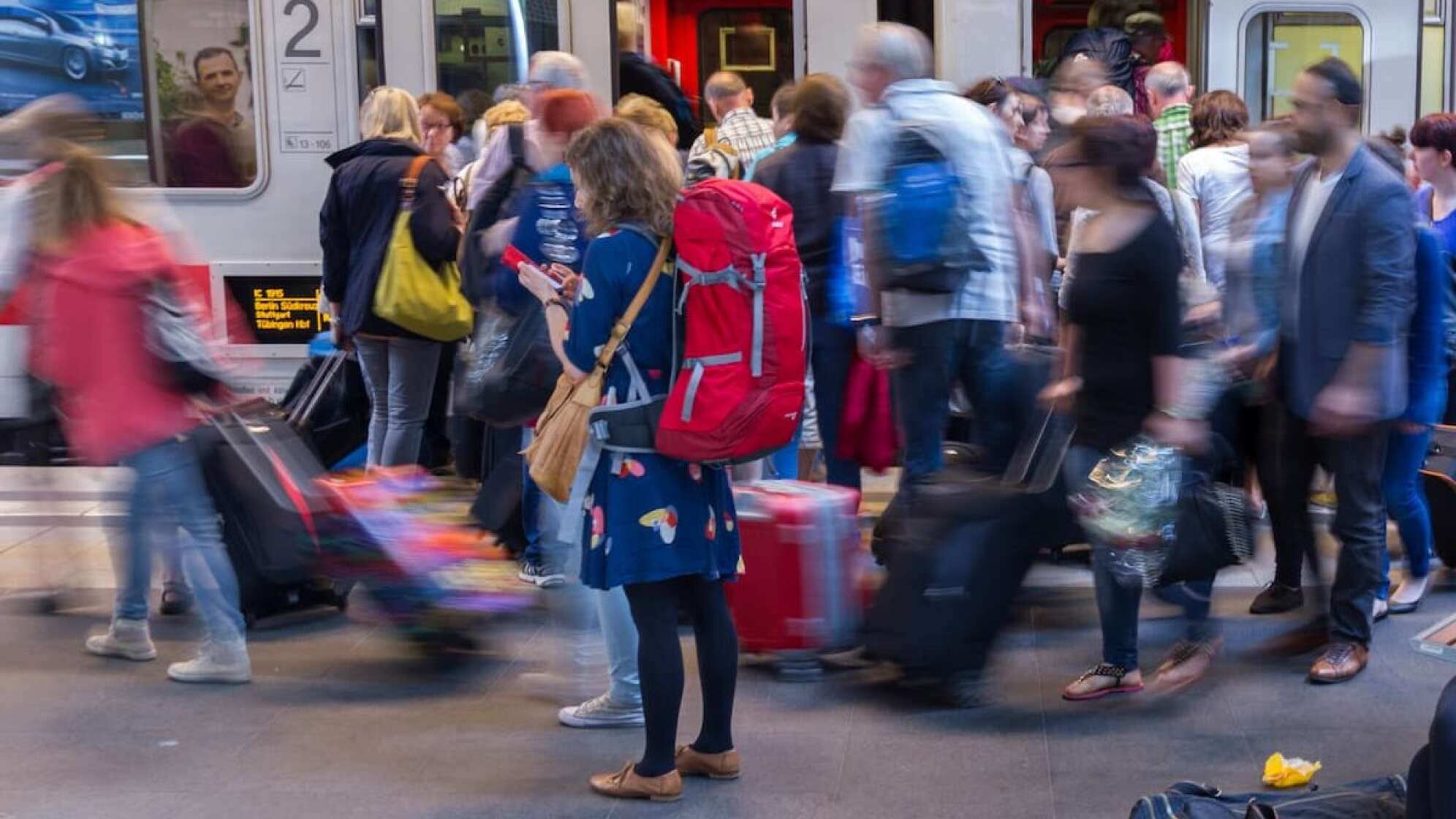 Menschenmenge am Bahnsteig, Frau mit Smartphone und großem Rucksack