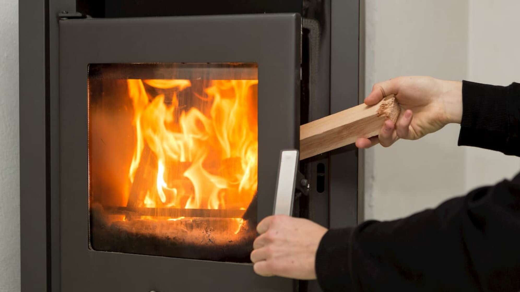 Mann heizt einen Kamin mit einem Stück Holz