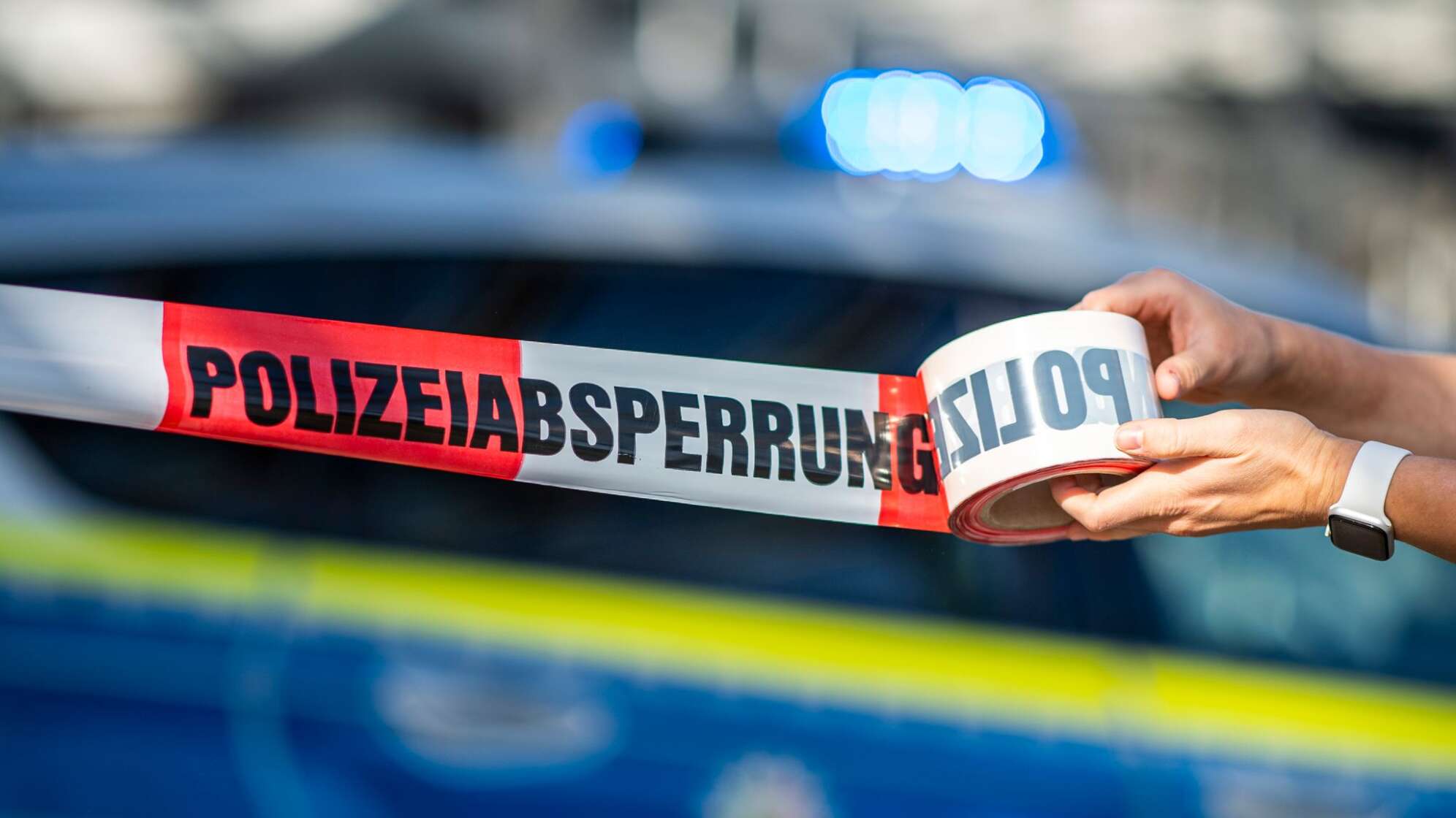 Eine Polizistin rollt ein Absperrband aus