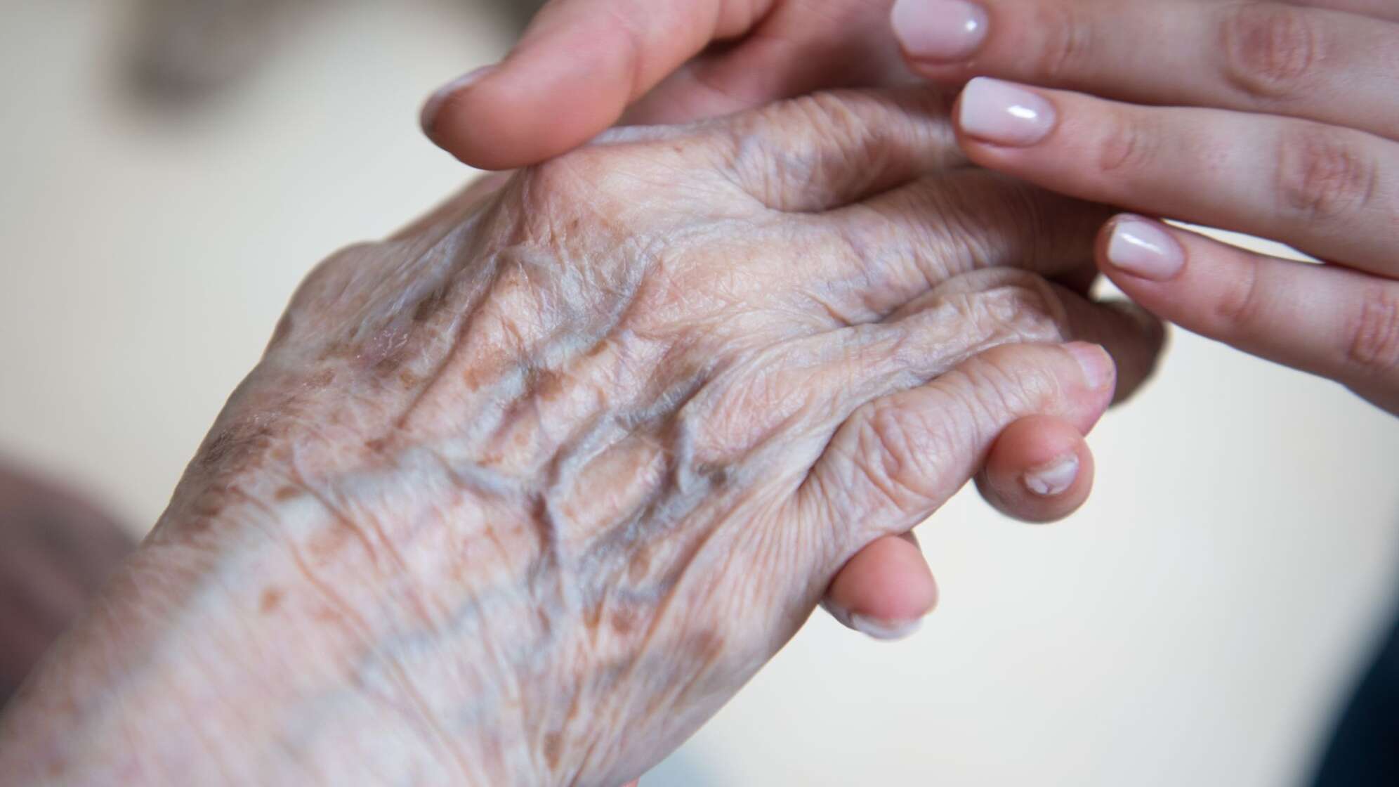 Pflegerin hält Hand einer Seniorenheim-Bewohnerin