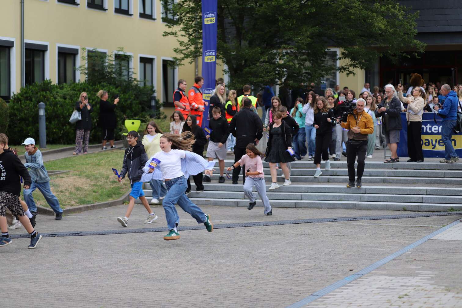 Popstar LOI am 23.07.2026 live auf der Bühne beim zweiten ANTENNE BAYERN Schulhof-Gig 2026 auf dem Pausenhof der Staatlichen Realschule in Neustadt bei Coburg in Oberfranken - Foto vom Konzert mit fröhlichen Schülern, hochgehaltenen Smartphones und Plakaten