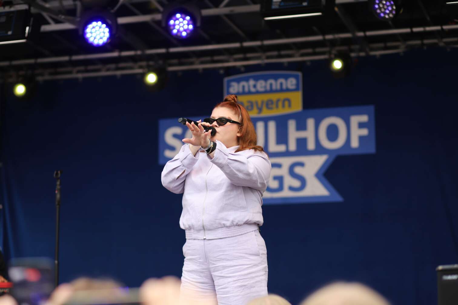 Popstar LOI am 23.07.2026 live auf der Bühne beim zweiten ANTENNE BAYERN Schulhof-Gig 2026 auf dem Pausenhof der Staatlichen Realschule in Neustadt bei Coburg in Oberfranken - Foto vom Konzert mit fröhlichen Schülern, hochgehaltenen Smartphones und Plakaten