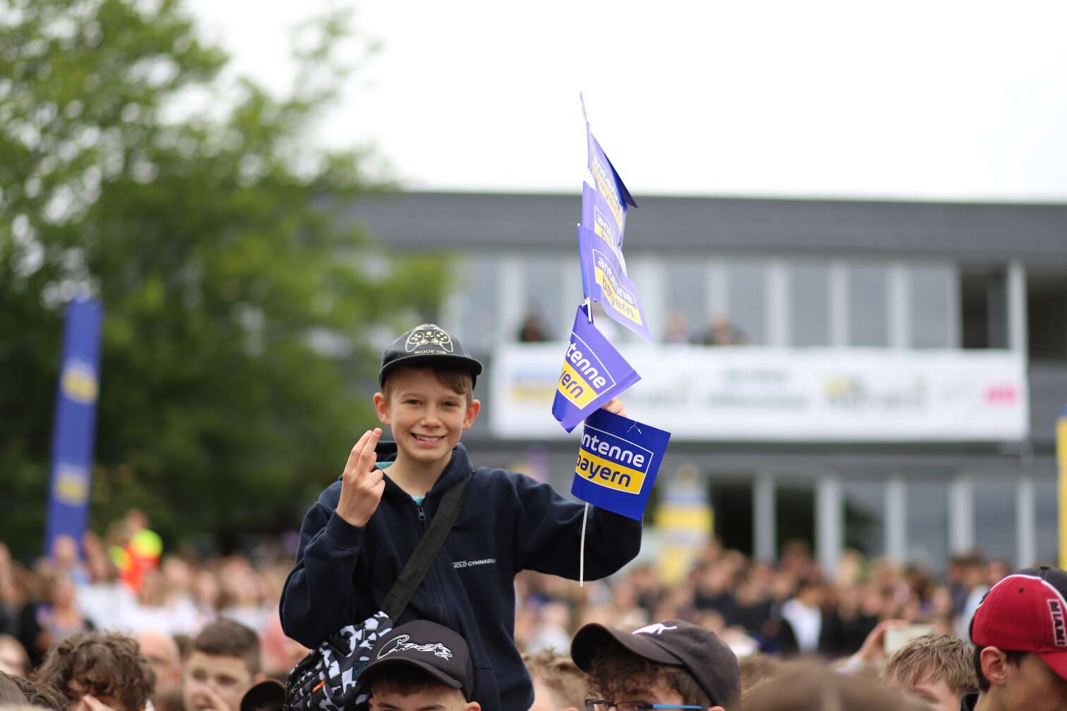 Popstar LOI am 23.07.2026 live auf der Bühne beim zweiten ANTENNE BAYERN Schulhof-Gig 2026 auf dem Pausenhof der Staatlichen Realschule in Neustadt bei Coburg in Oberfranken - Foto vom Konzert mit fröhlichen Schülern, hochgehaltenen Smartphones und Plakaten