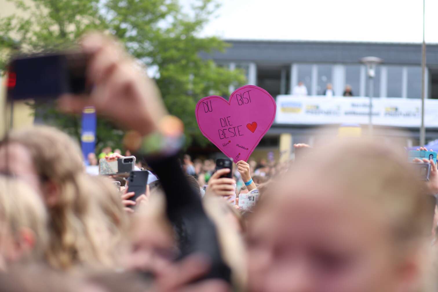 Popstar LOI am 23.07.2026 live auf der Bühne beim zweiten ANTENNE BAYERN Schulhof-Gig 2026 auf dem Pausenhof der Staatlichen Realschule in Neustadt bei Coburg in Oberfranken - Foto vom Konzert mit fröhlichen Schülern, hochgehaltenen Smartphones und Plakaten