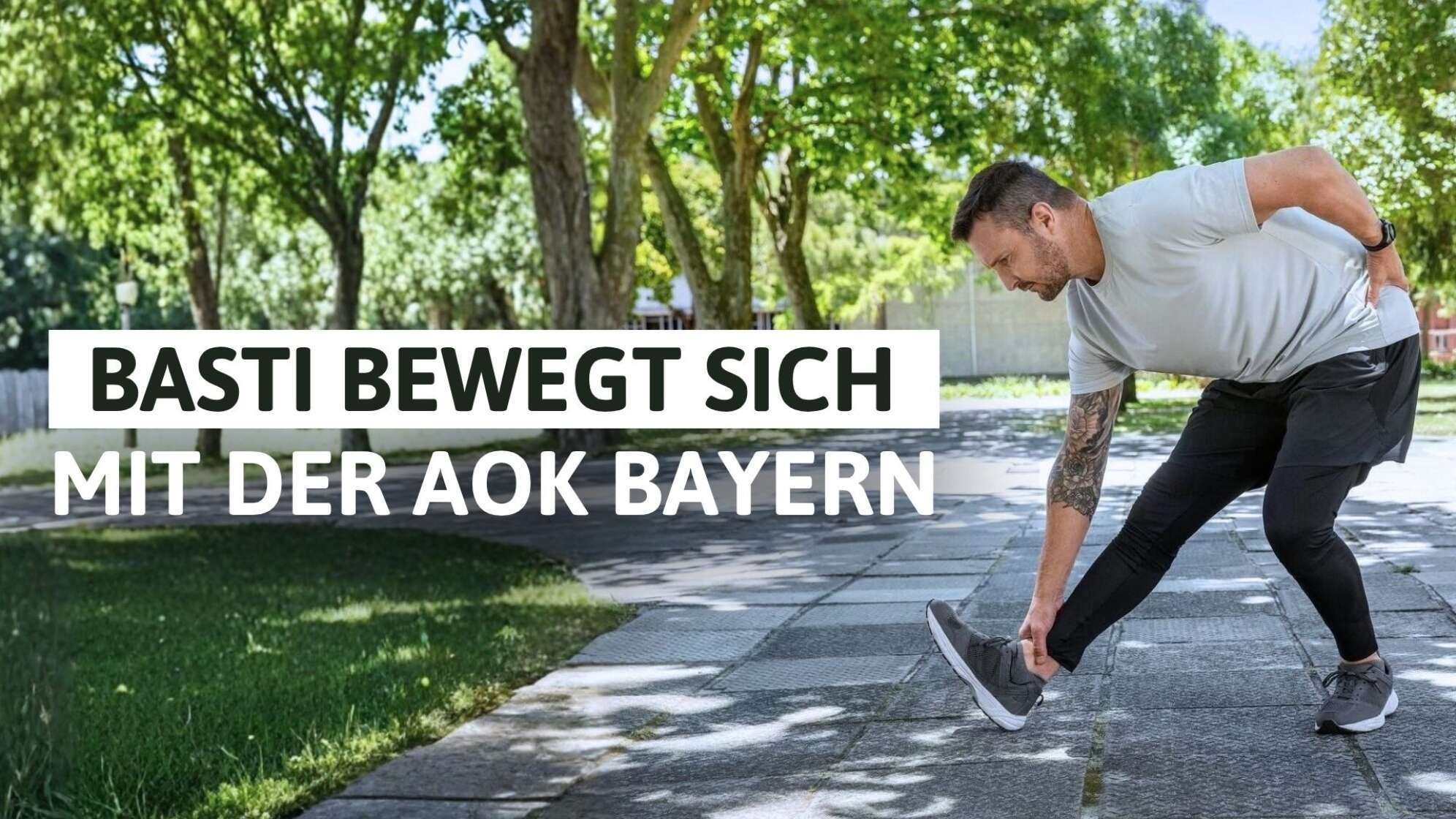 Gesundheitskampagne „Basti bewegt sich mit der AOK Bayern“: Mann in Sportkleidung macht Dehnübung auf einem sonnigen Weg im Park, links große weiße Schrift „Basti bewegt sich mit der AOK Bayern“ – Aktion für mehr Bewegung und Fitness in Bayern.