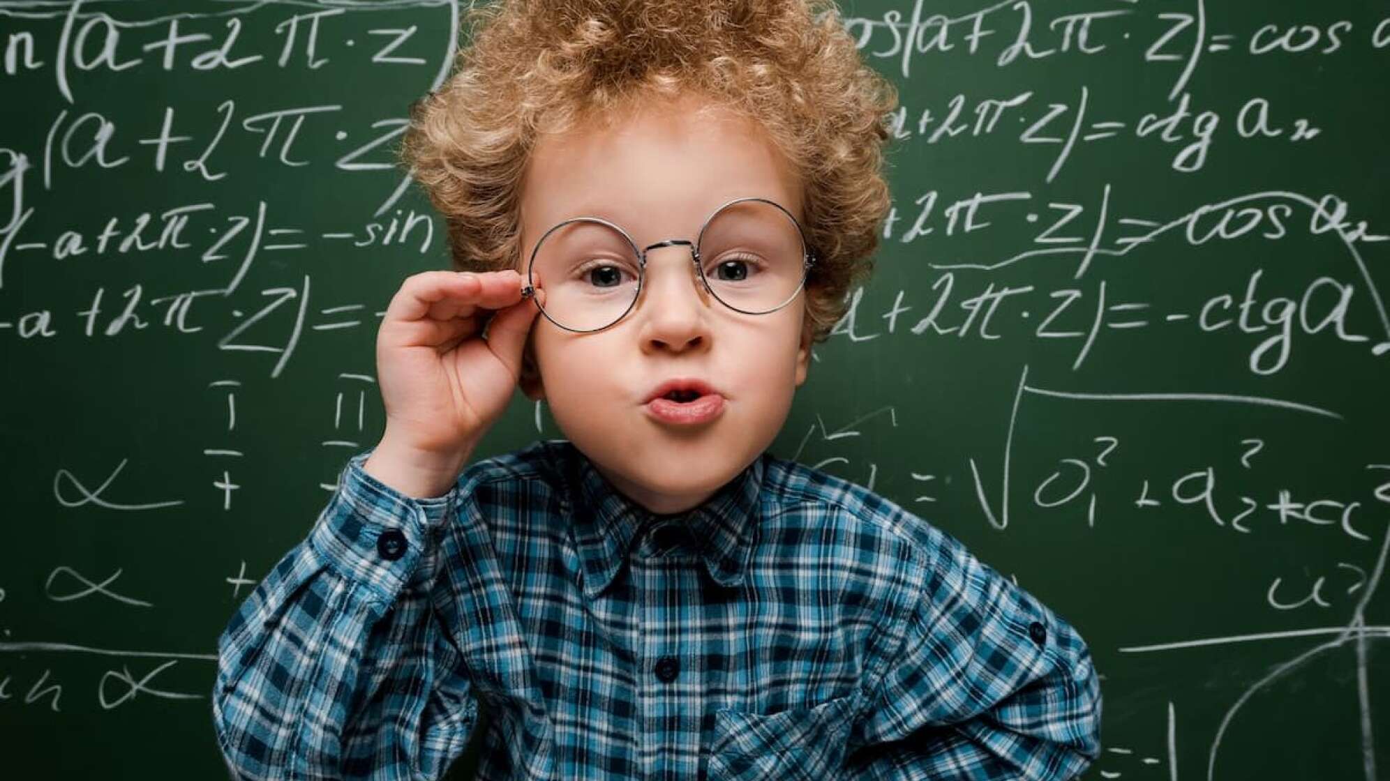Kind mit Brille und Struppelhaaren vor beschriebener Tafel