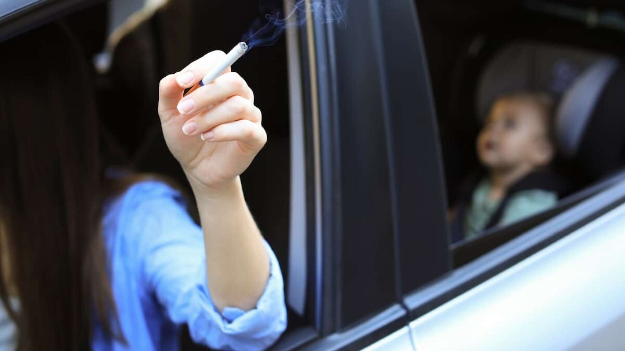 Hand mit Zigarette im Auto mit Baby
