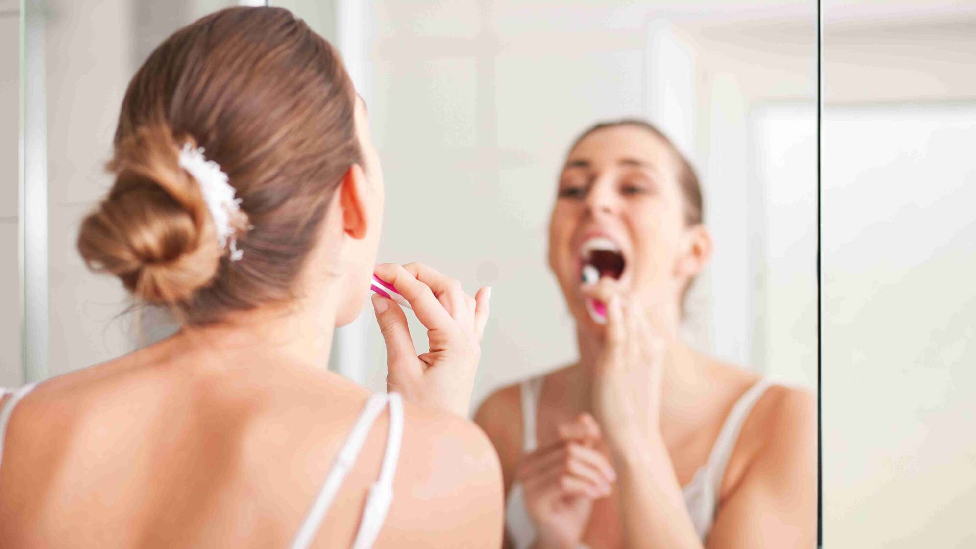 Frau putzt Zähne vor dem Spiegel