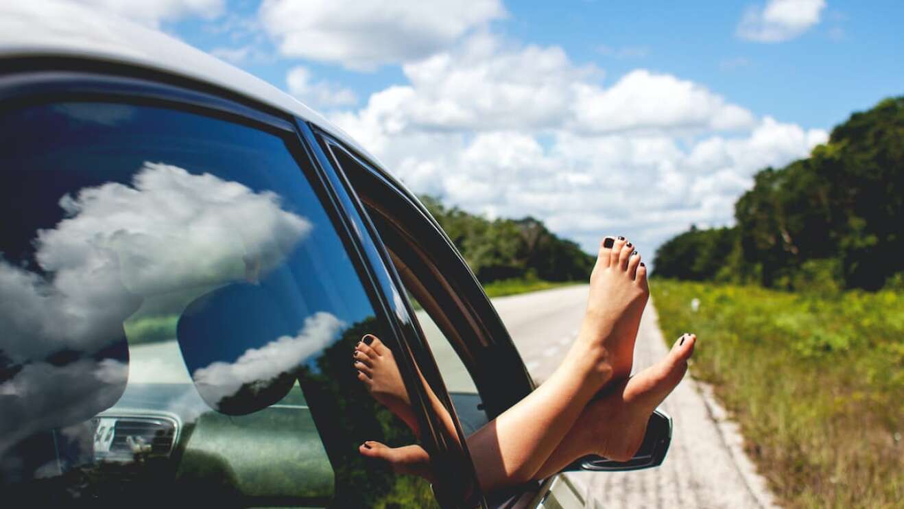 Eine Frau hängt ihre Füße aus dem Autofenster.
