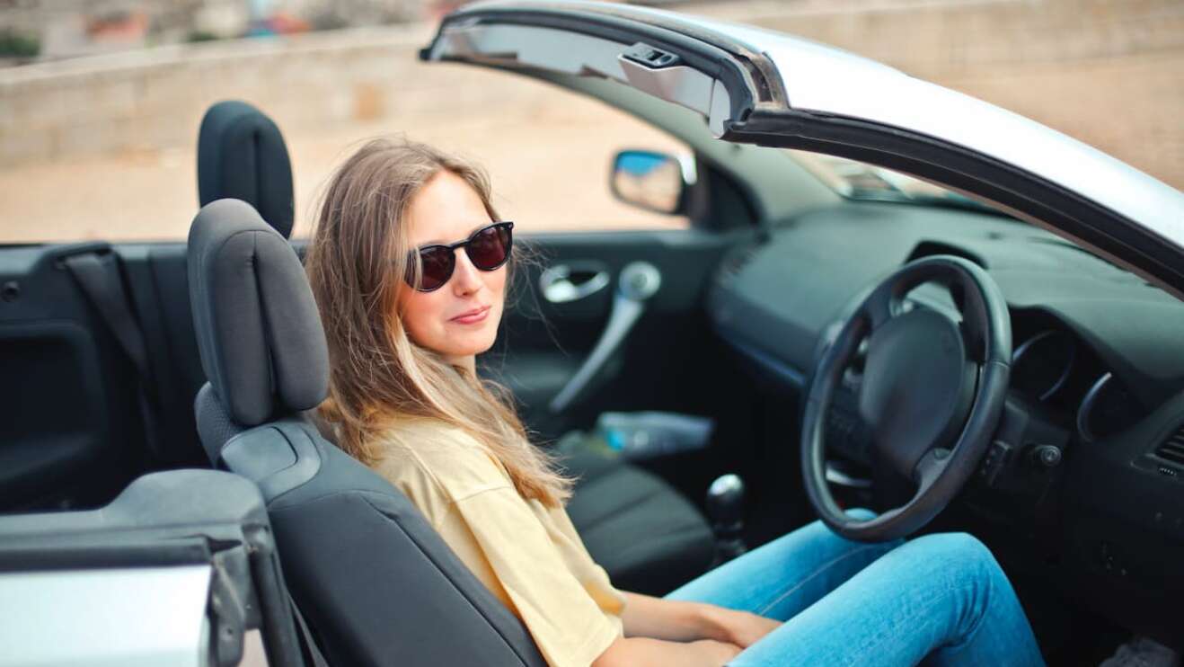 Eine Frau mit Sonnenbrille sitzt in einem Cabrio.