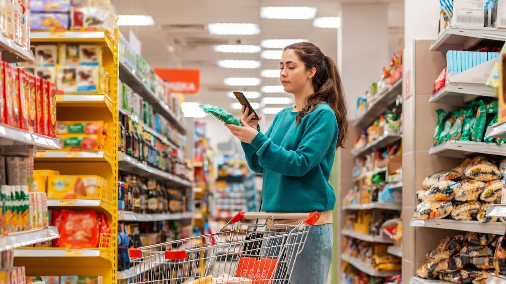 Frau im Supermarkt schaut auf ihr Handy
