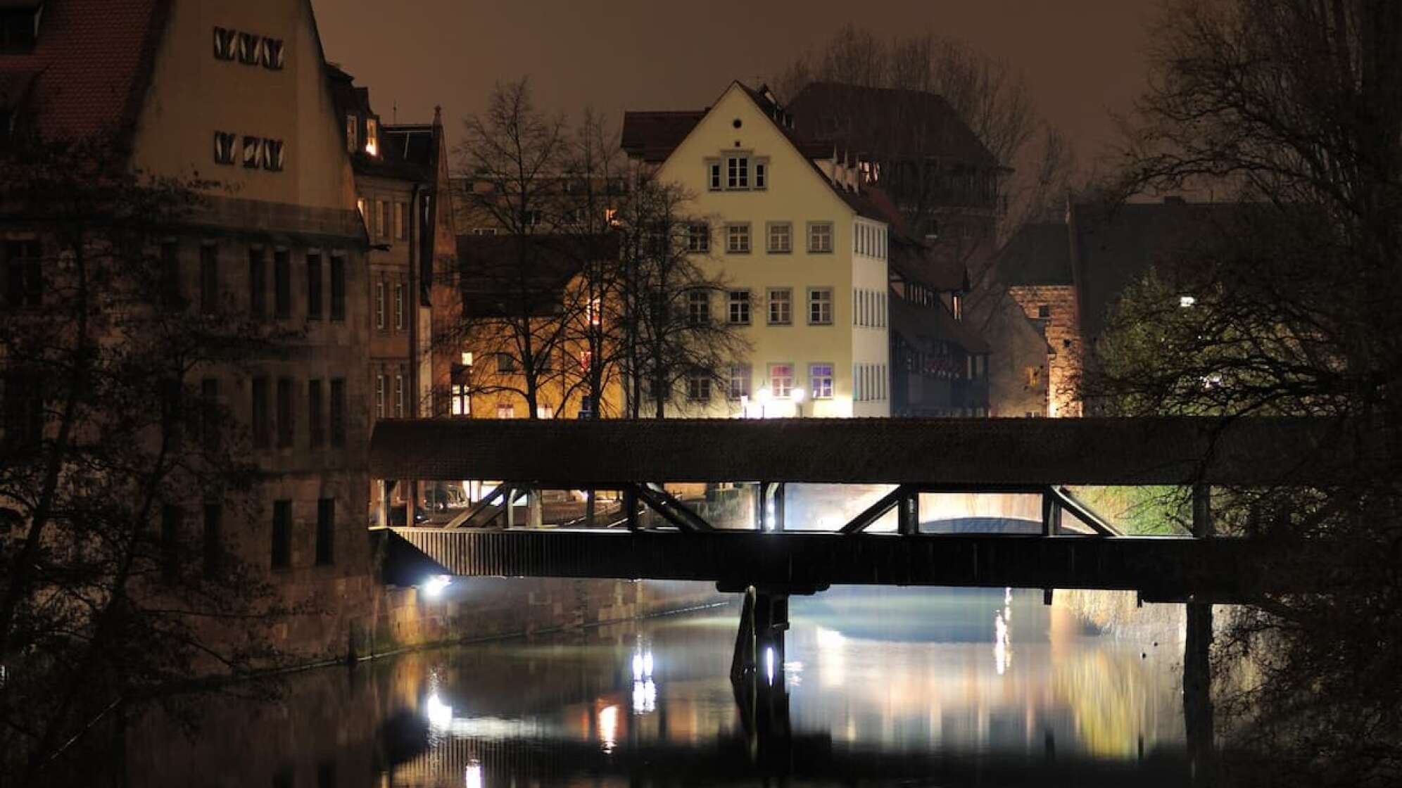 Häuser in Dunkelheit mit Gewässer und angestrahlter Brücke