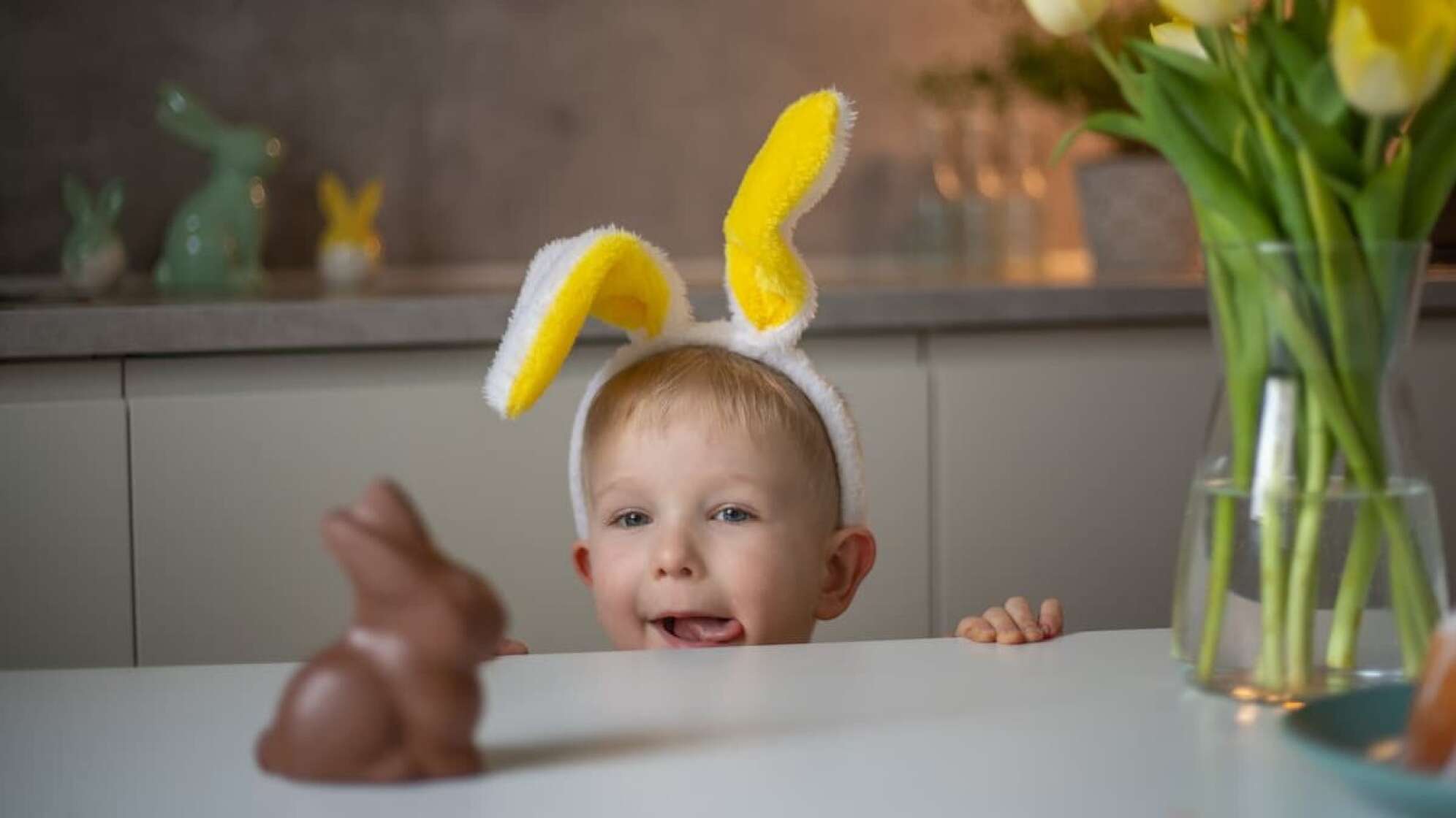 Eine Junge mit Hasenohren, der auf einen Schokohasen blickt