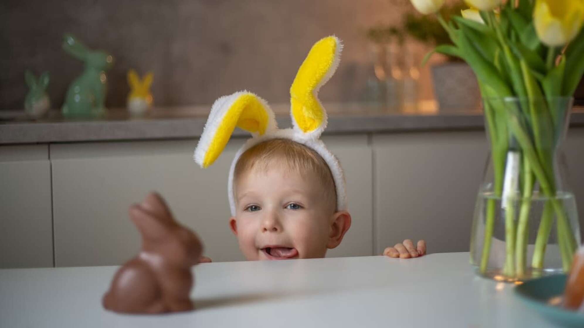 Eine Junge mit Hasenohren, der auf einen Schokohasen blickt