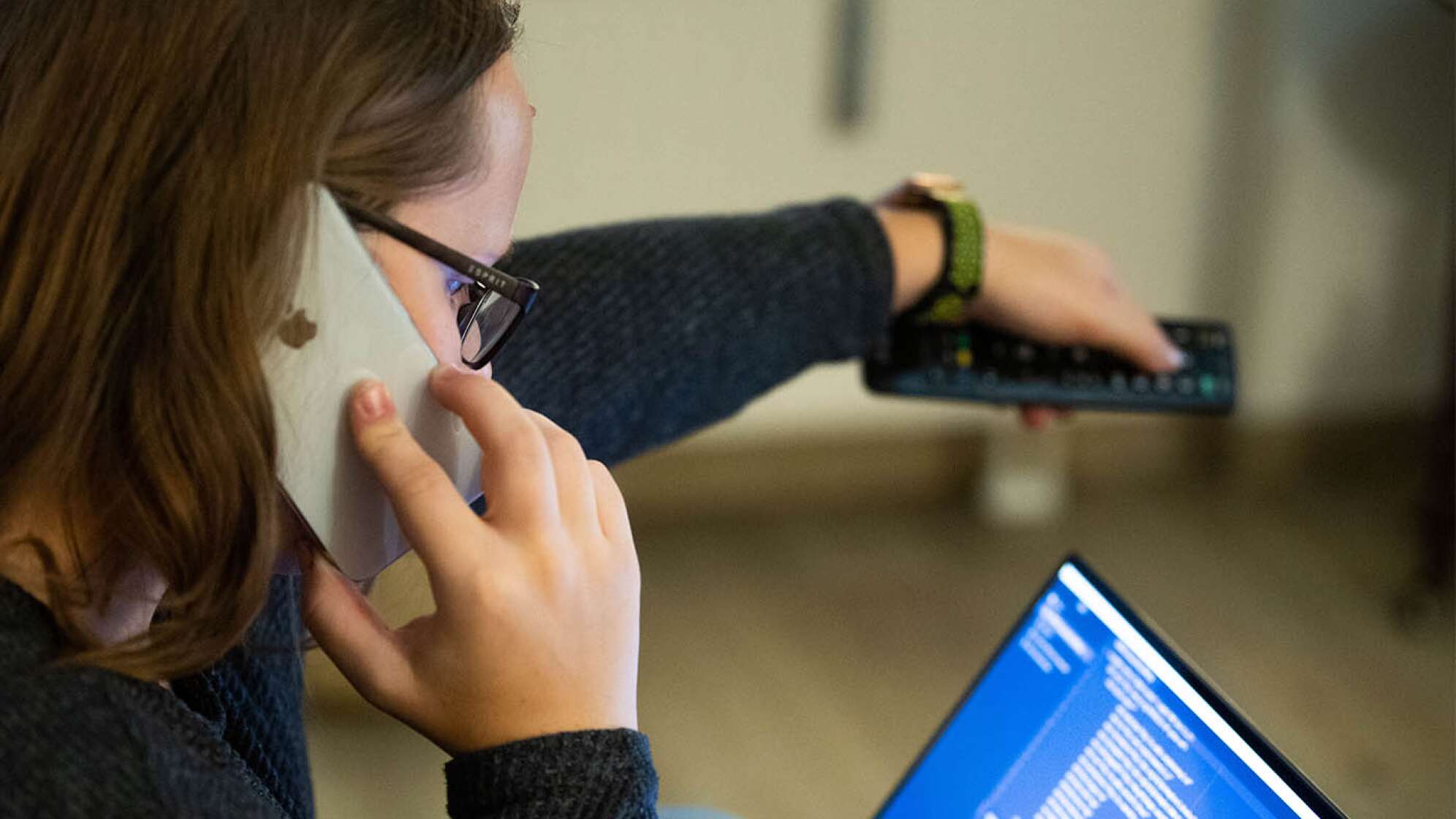 Eine Frau, die telefoniert, in einen Laptop schaut und eine Fernbedienung benutzt