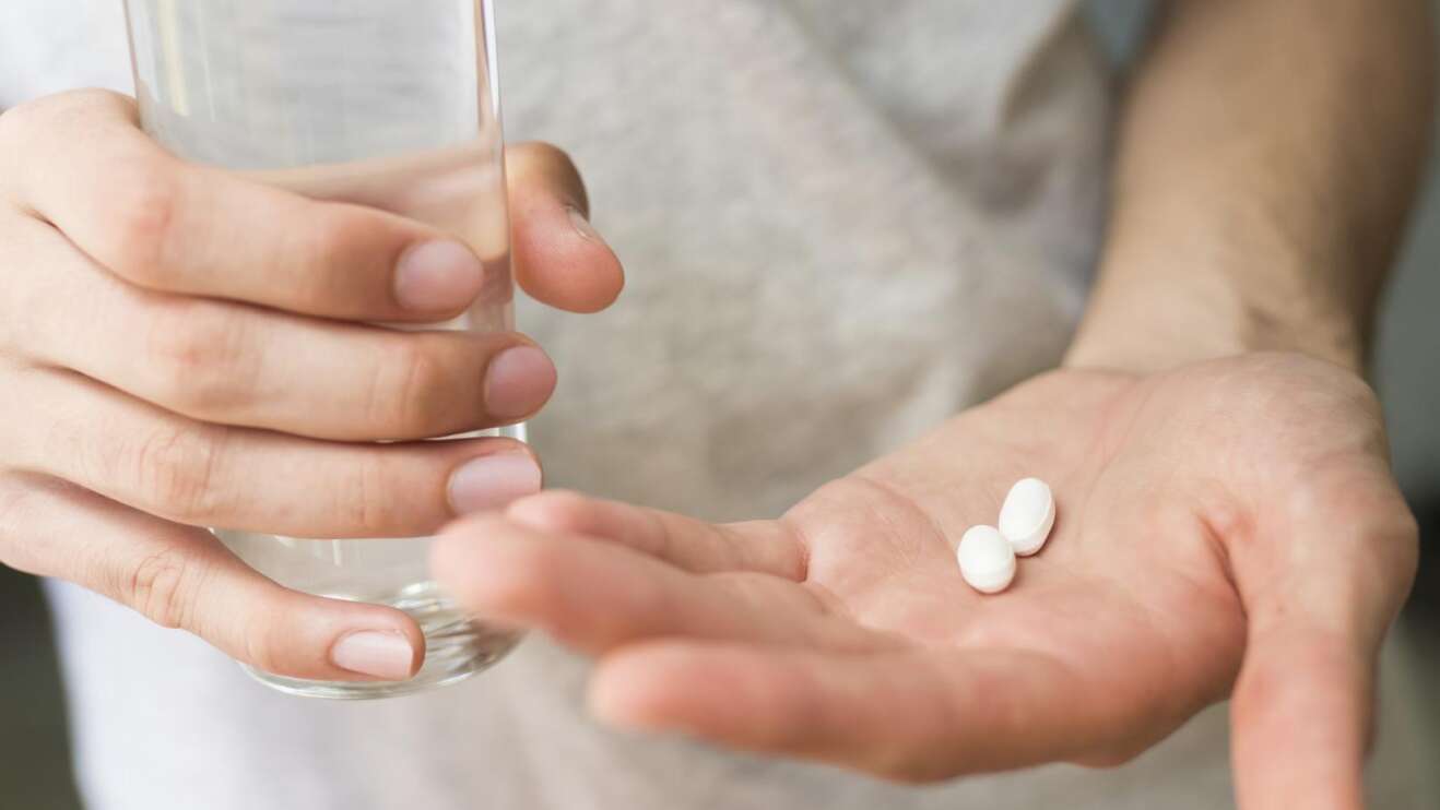 Eine Person hält eine Glas Wasser und Pillen in der Hand