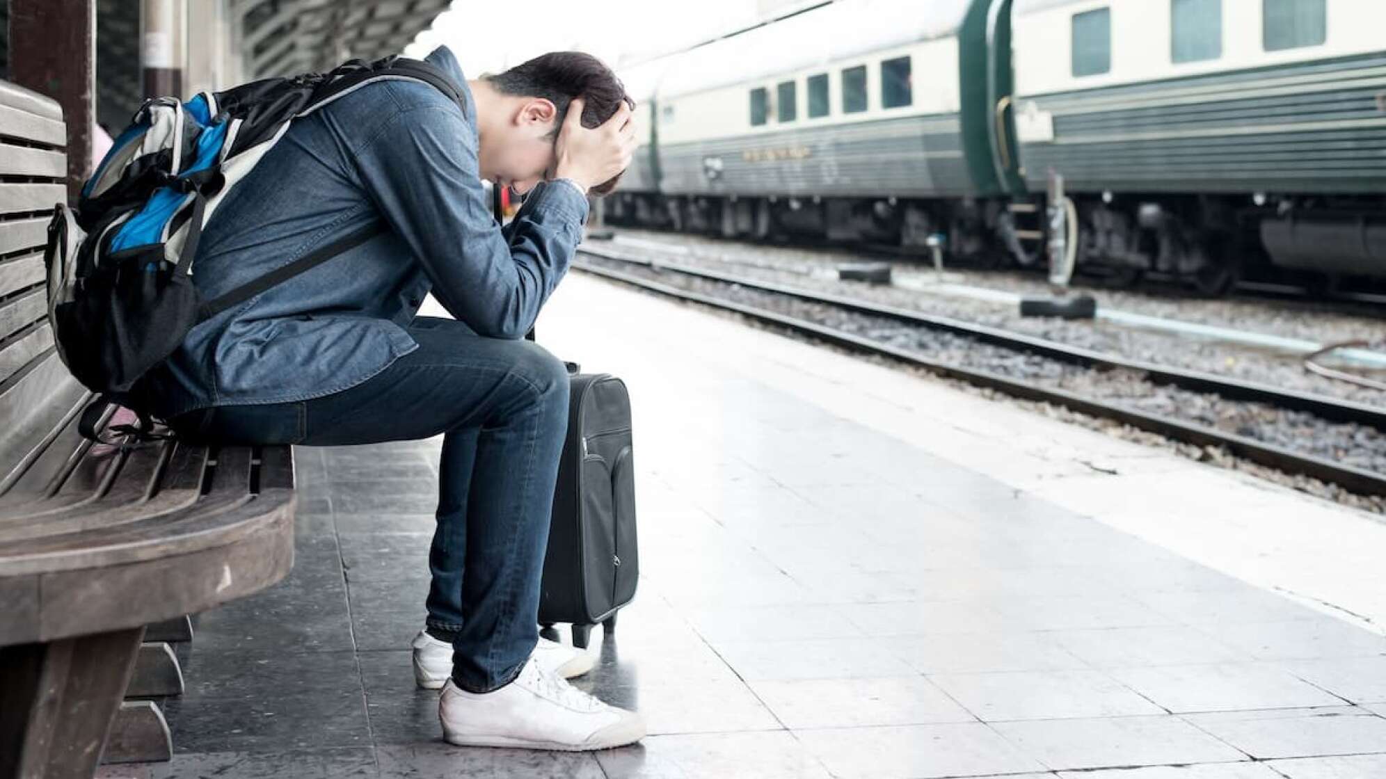 Mann sitzt mit Gepäck an einem Bahnsteig