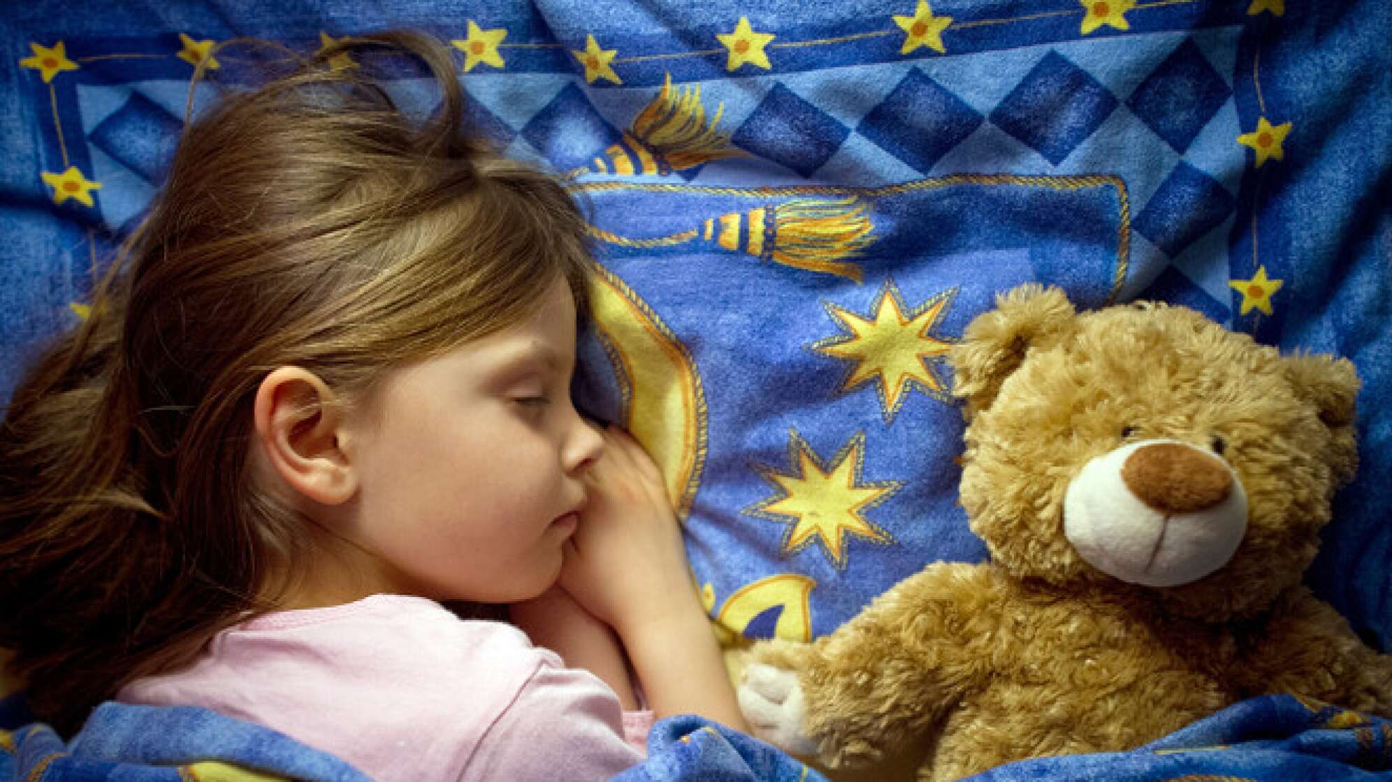 Kind schläft im Bett neben Teddy