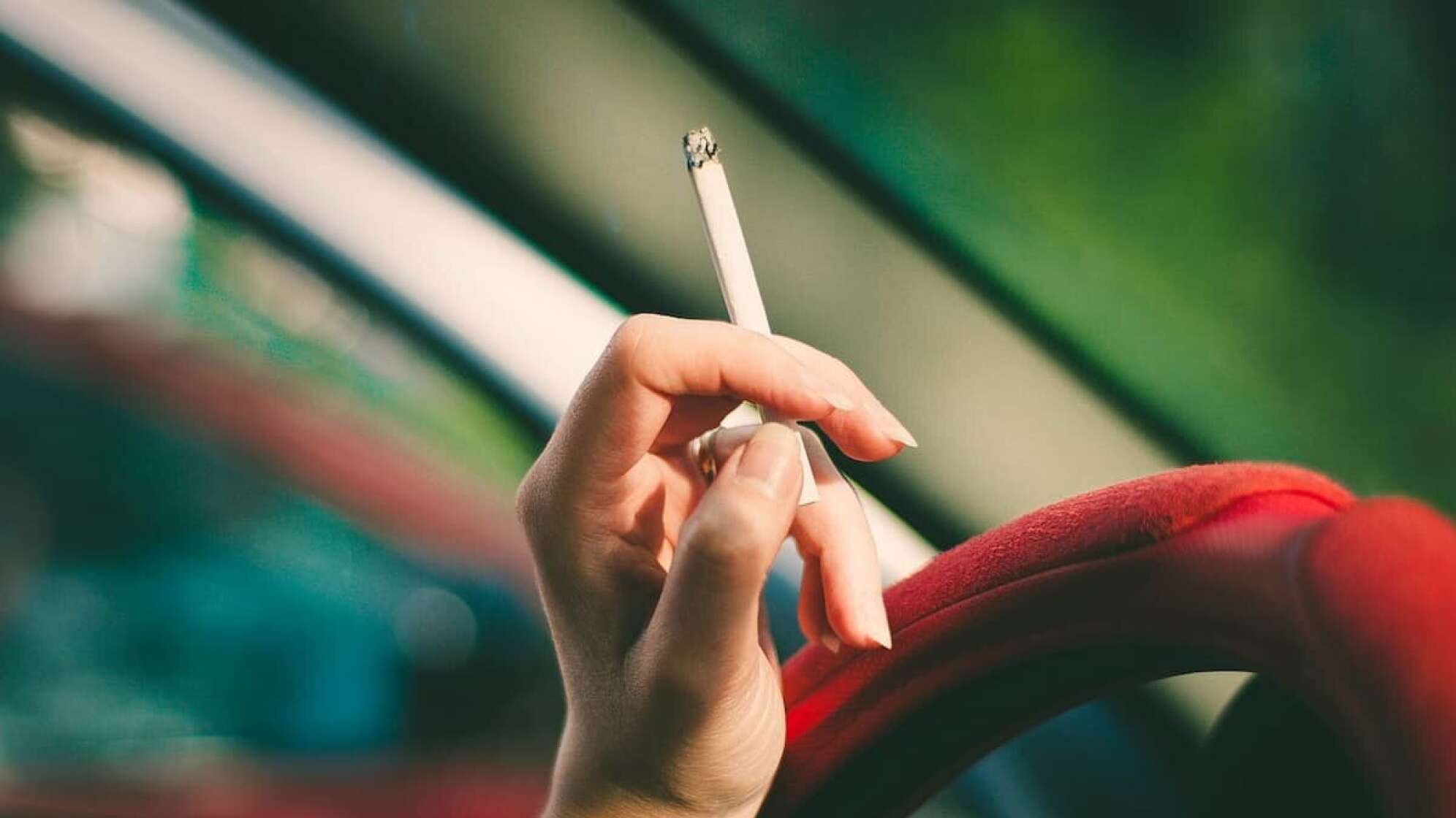 Eine Hand am Lenkrad, die eine Zigarette hält