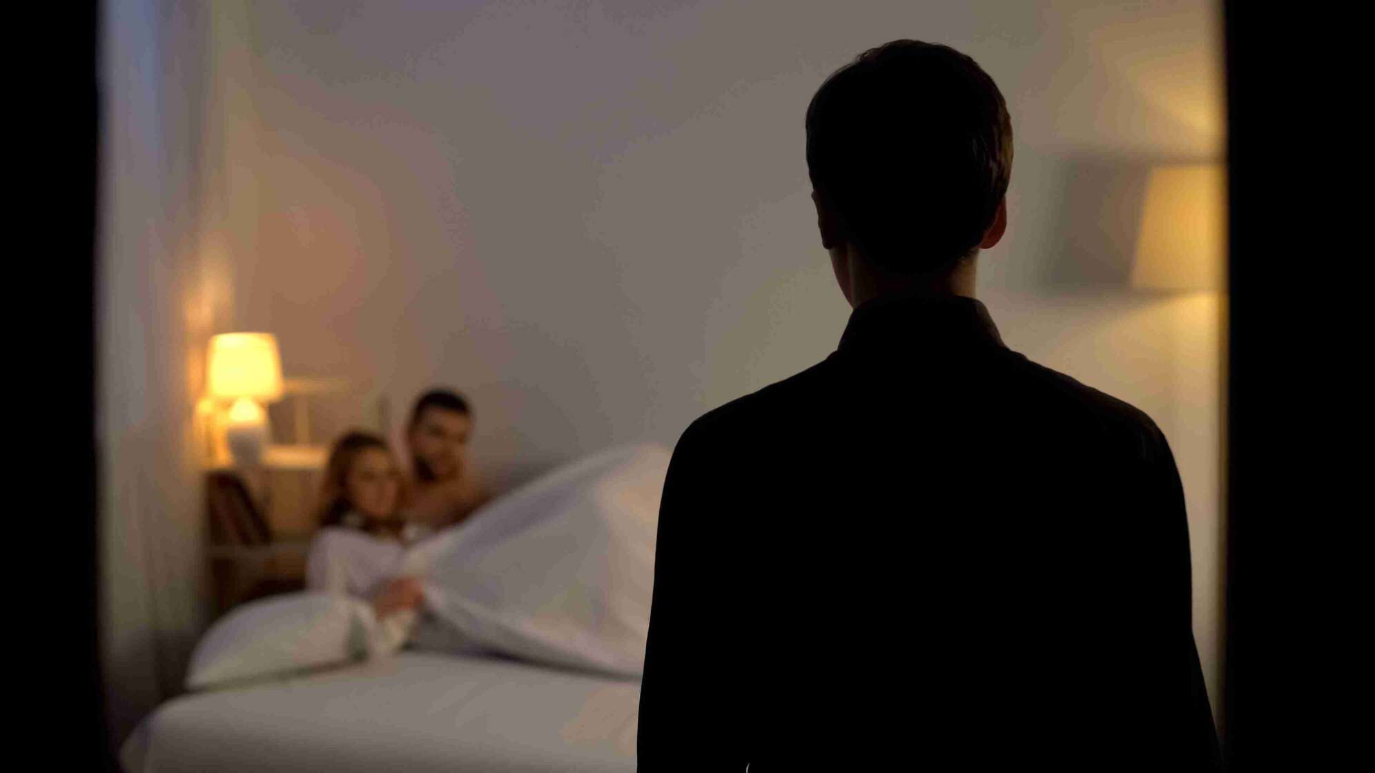 Mann sieht Frau mit Mann im Bett