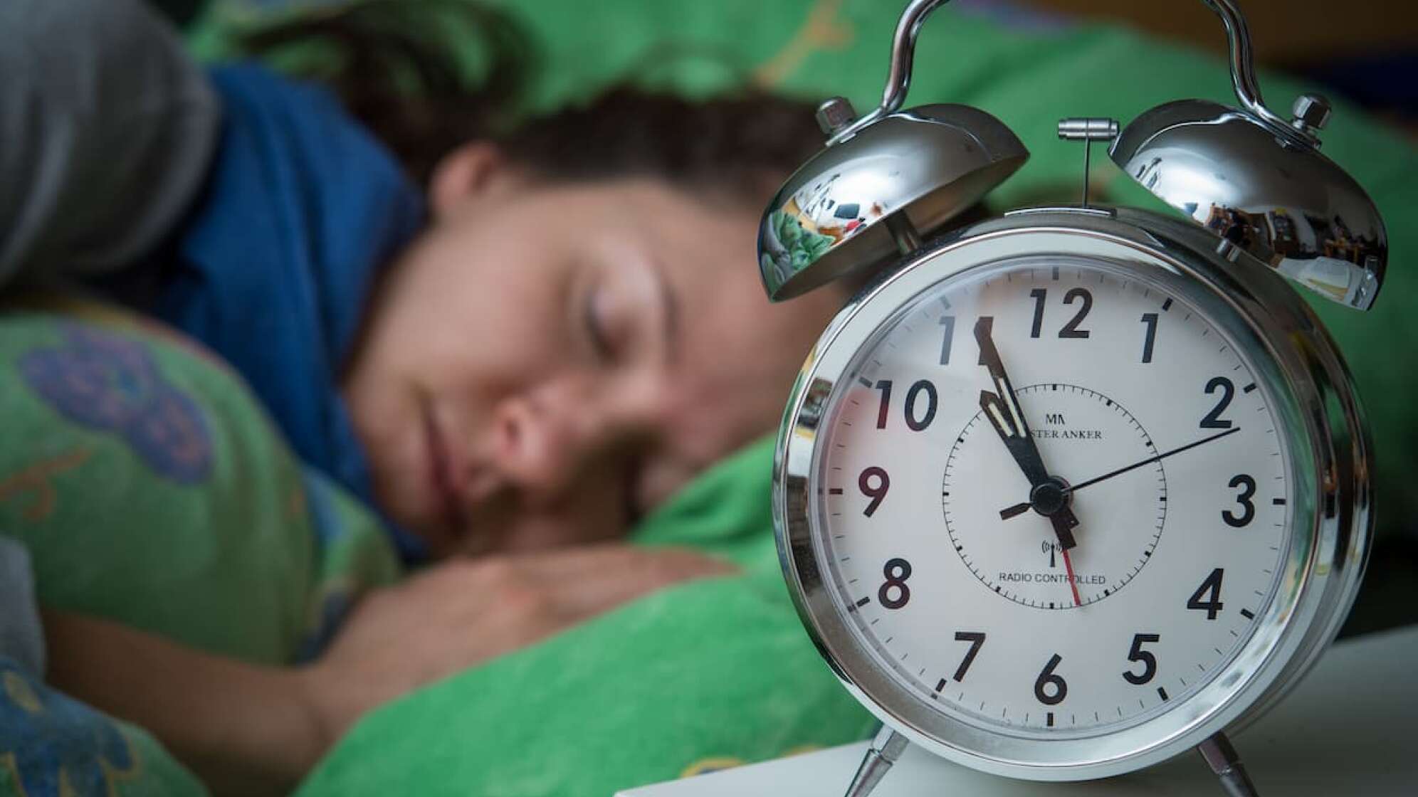 Wecker mit schlafender Frau im Hintergrund