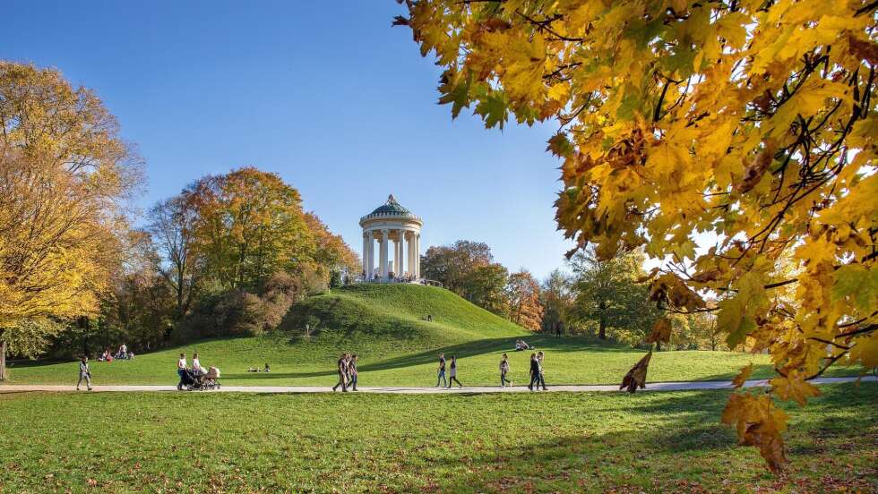 Englischer Garten in München mit grünen Wiesen, Bäumen und Spaziergängern bei sonnigem Wetter.