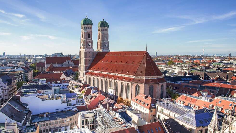 Frauenkirche in München mit markanten Zwillingstürmen und grünen Kuppeln, umgeben von Stadtlandschaft.